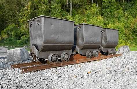 Three mining carts on a rail on the rocks in the sunny day near forest